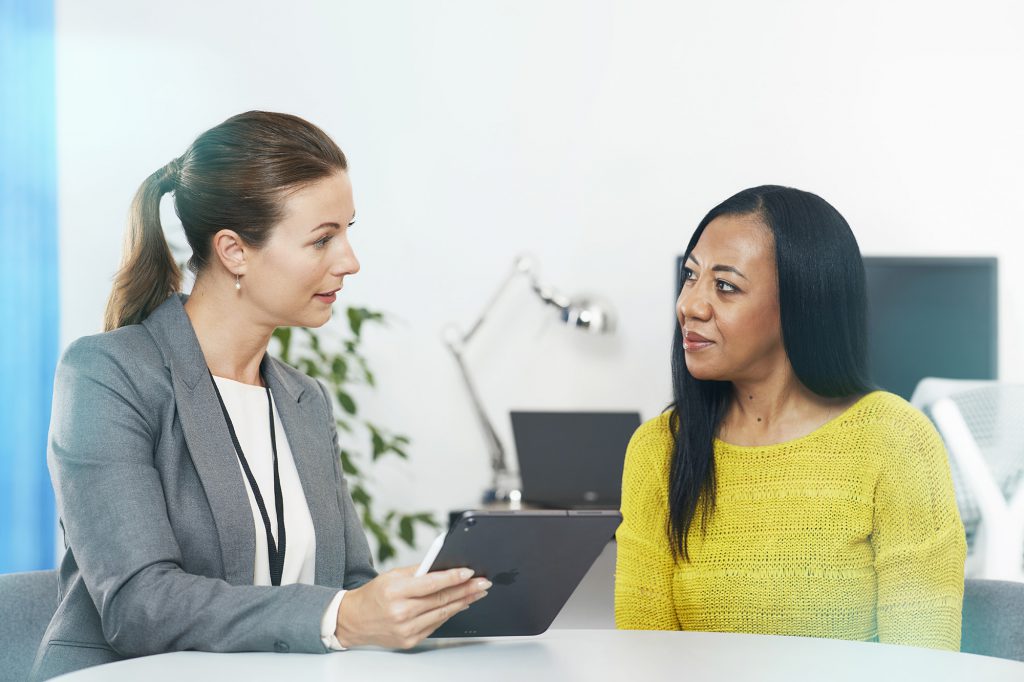 A health professional holding a clipboard talking with a patient